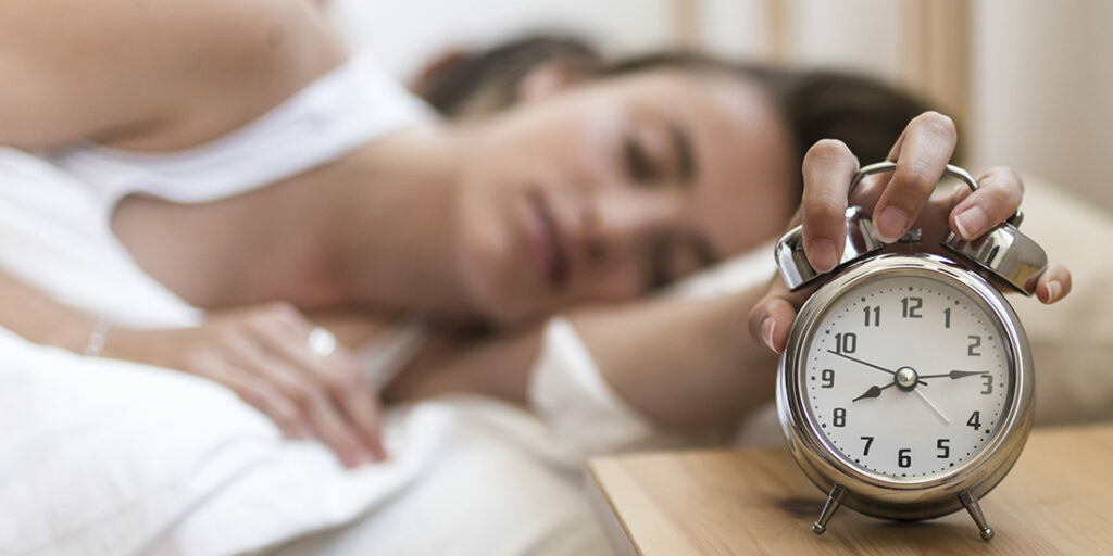 woman-sleeping-bed-turning-off-alarm-clock