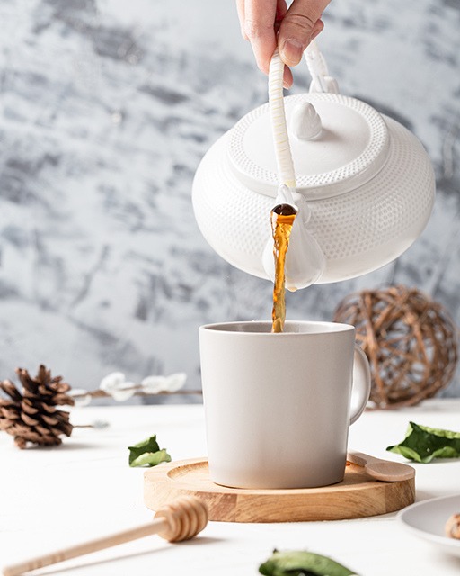 Vertical shot of a tea pouring from a kettle to a white cup with a wooden spoon