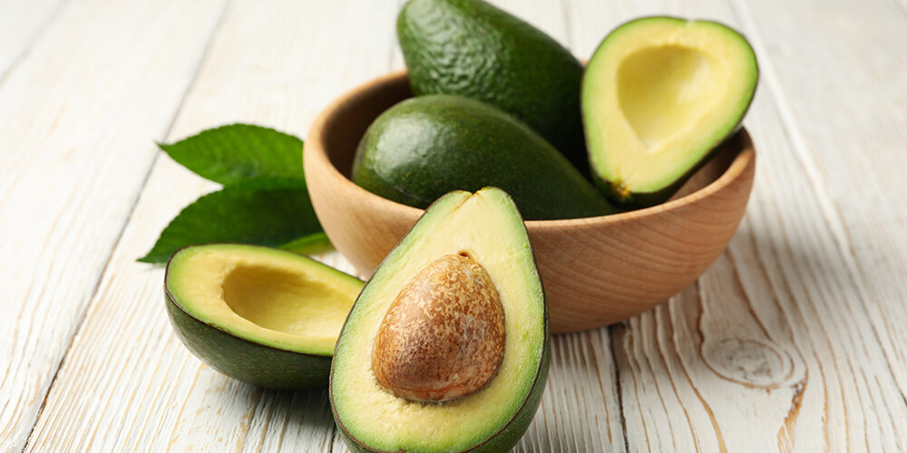 Bowl with fresh avocado on wooden background, close up