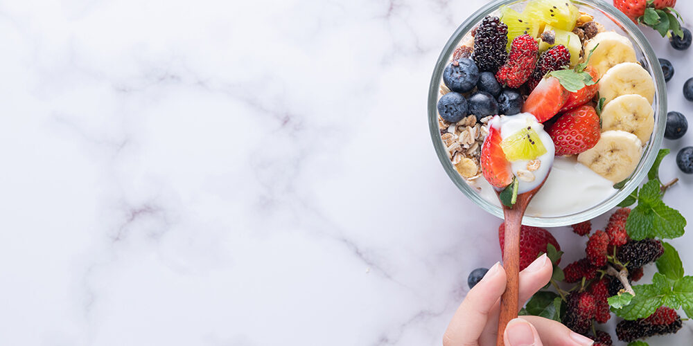 Homemade muesli, bowl of oat granola with yogurt, mint and nuts board for healthy breakfast, copy space. Healthy breakfast menu concept. spoon in women's hands. Clean eating, dieting, detox.