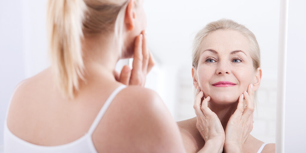 Beautiful woman looking at wrinkles in mirror