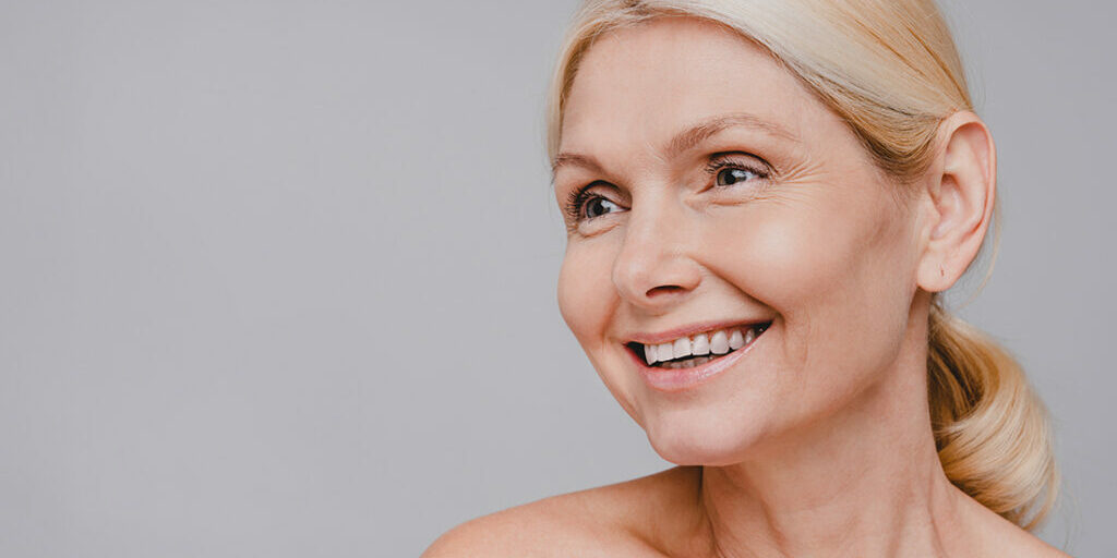 Side view cropped portrait of good-looking middle-aged woman with fresh face isolated over grey background