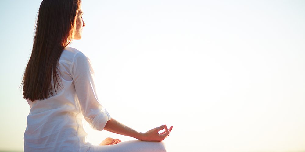 Side view of meditating woman sitting in pose of lotus against clear sky outdoors